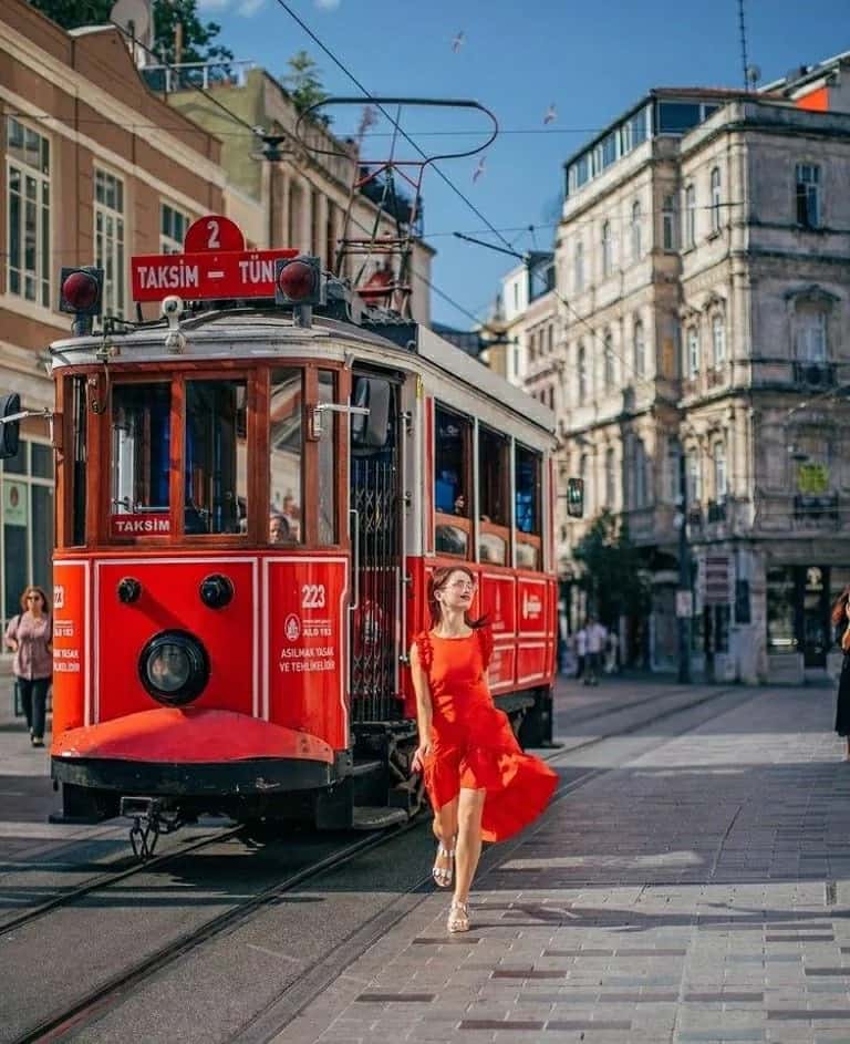Woman in a red dress walking beside the historic Taksim tram